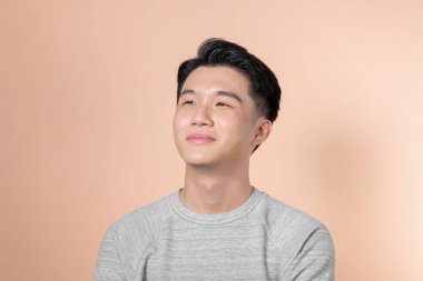 Bej arka planda izole edilmiş gülümseyen Asyalı genç adamın yakışıklı portresi.