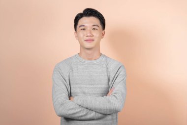 Kolları çaprazlanmış sıradan bir adam bej arka planda izole edilmiş.