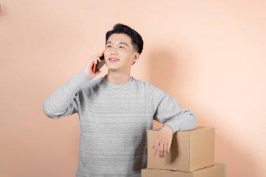 Paketlerle ayakta dururken Asyalı teslimatçı cep telefonu kullanıyor..