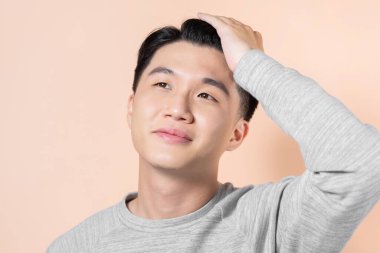 Bej arka planda saçına dokunan Asyalı bir adamın portresi.