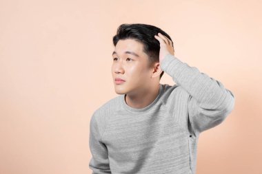 Saçına dokunan bir adamın portresi bej arka planda izole bir şekilde duruyor.