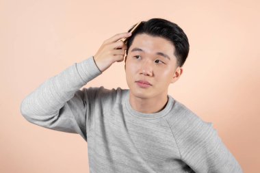 Çekici Asyalı adam bej arka planda saçını tarıyor.