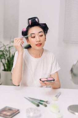 Çekici bir kadın aynanın yanında yüzüne göz farı sürüyor. 