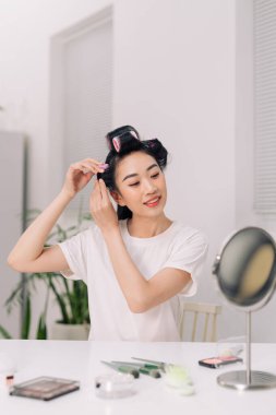 Oturma odasının arka planında izole edilmiş saç maşalı mutlu güzel bir kadının portresi.