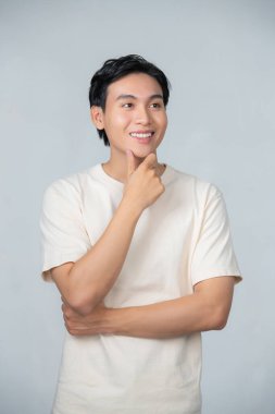 Asyalı bir adam eli çenesinde kameraya bakıp mutlu bir yüz takınıyor.