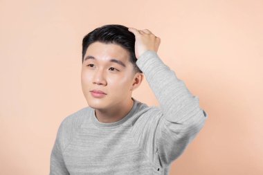 A chic impressive man with a stylish hairstyle, looks into the camera and touches his hair.