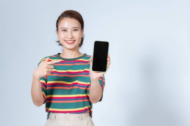 A smiling woman is pointing on smartphone standing on white background.