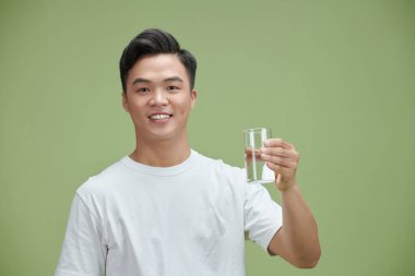 Handsome young man in a white T-shirt holding a glass of drinking water