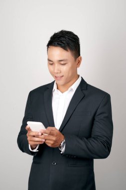 Young smiling handsome Asian man in formal suit using mobile phone on white