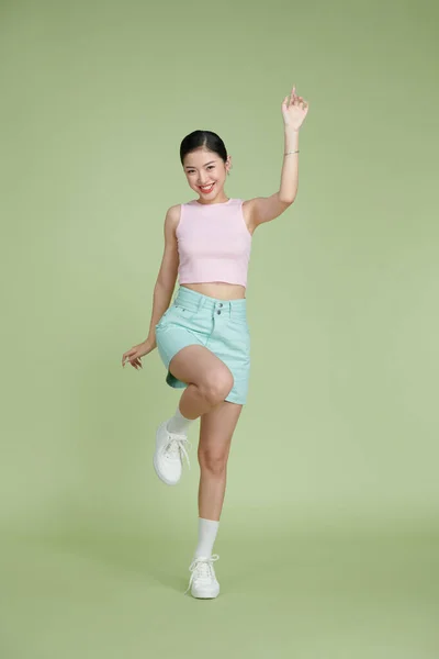 Full body of happy girl dancing your hands up on green pastel background