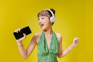 Kablosuz kulaklıkla müzik dinleyen ve elinde cep telefonu tutan sevimli trend kadının fotoğrafı.