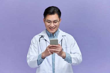 Mor arka planda izole edilmiş akıllı bir telefondan mesaj atan mutlu doktor.