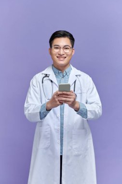 Mor arka planda izole edilmiş akıllı bir telefondan mesaj atan mutlu doktor.