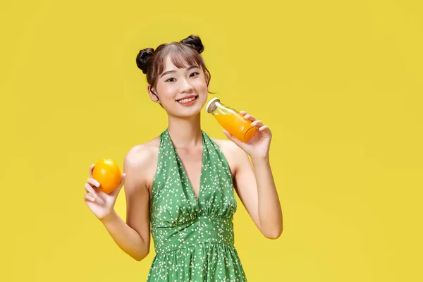 興奮アジア人女性飲料新鮮なオレンジジュースグラス黄色の背景に立って — ストック写真