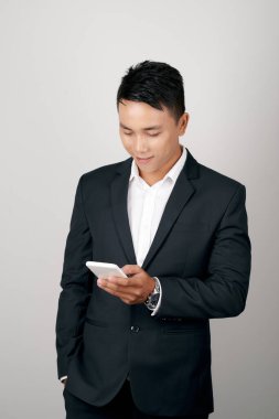 Young smiling handsome Asian man in formal suit using mobile phone on white
