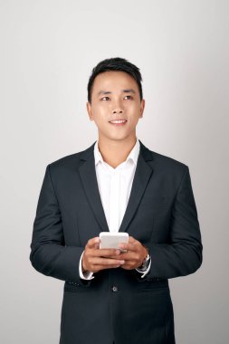 Young smiling handsome Asian man in formal suit using mobile phone on white