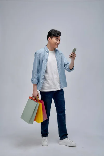 Ung Asiatisk Man Med Shoppingväskor Använder Mobiltelefon Och Ler När — Stockfoto