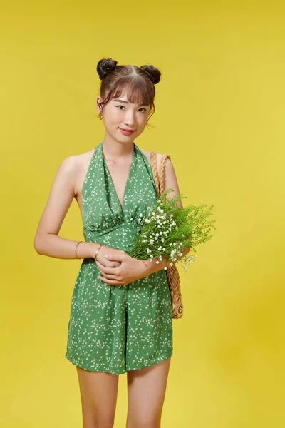 Photo of nice young asian lady hold flowers wear summer clothes isolated on yellow background