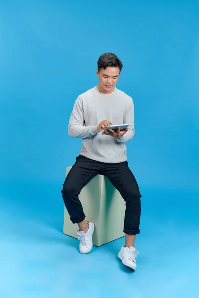 Jovem Feliz Sentado Cubo Geometria Usando Tablet Sobre Fundo Azul — Fotografia de Stock