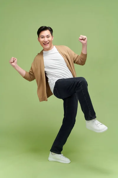 快乐而兴奋的年轻亚洲男人在绿色工作室的背景下独自跳跃 — 图库照片