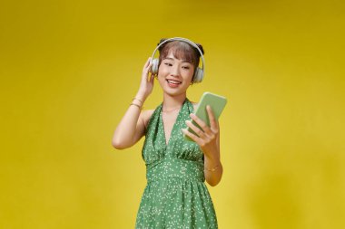 Cep telefonundan müzik dinleyen kulaklık takan mutlu Asyalı kız.