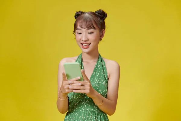 用手机发笑 用黄色背景孤立地输入短信的年轻女子的画像 — 图库照片