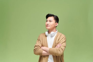 Asyalı yakışıklı genç adam elleri bağlı, kulaklıkla ayakta duruyor ve gülümsüyor.