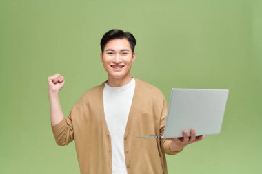 Mutlu Asyalı adam dizüstü bilgisayarını tutuyor ve başarıyı kutlamak için kolunu kaldırıyor. 