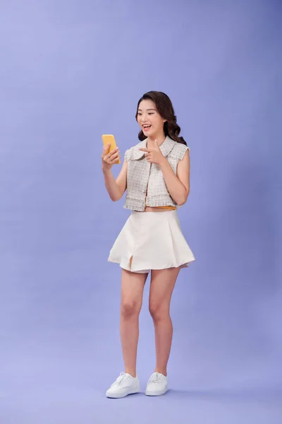 一位年轻美丽的亚洲微笑的女人拿着手机 用手指指着屏幕 — 图库照片