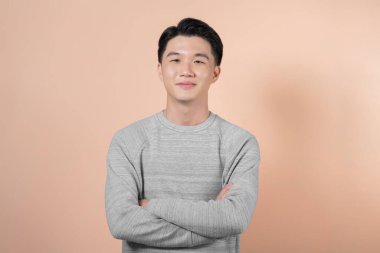 Kolları çaprazlanmış yakışıklı, neşeli Asyalı adamın belden yukarı portresi. Bej arka planda izole edilmiş.