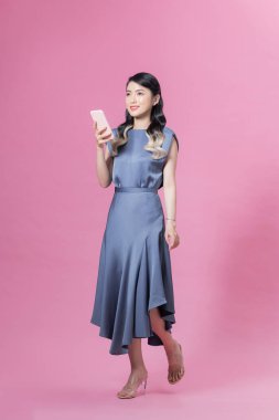 Güzel bir kadın pembe arka planda cep telefonu sohbeti yapıyor.