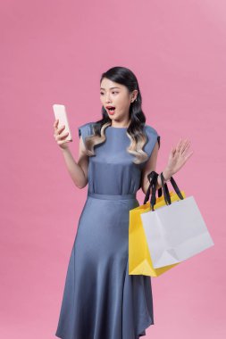 Şok olmuş ve heyecanlı alışveriş kadını pembe izole edilmiş arka planda akıllı telefon uygulaması kullanıyor.