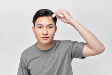 Yakışıklı, neşeli adam, yüzü için besleyici serum kullanıyor.