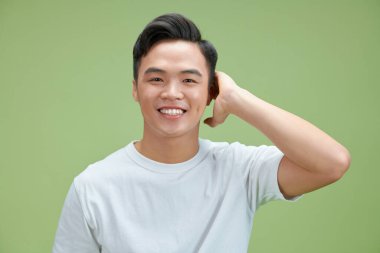 Çekici bir adam yeşil duvarın arkasında saçına dokunuyor.