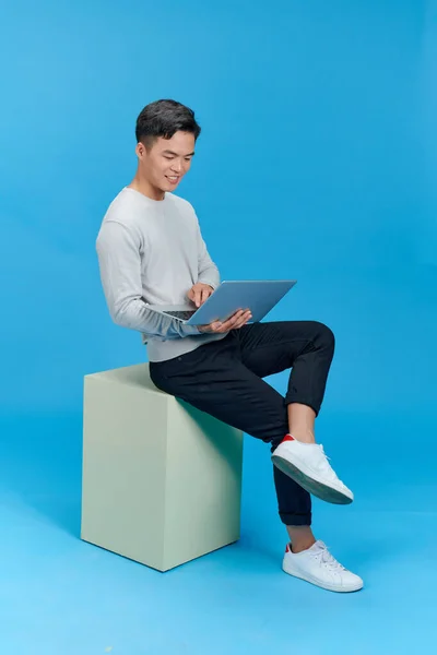 stock image Full length profile photo of attractive young man sitting on cube with laptop