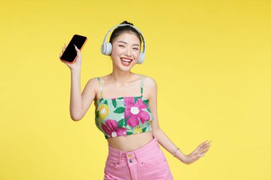 Kulaklık takan neşeli, hoş bir kadın. Modern teknoloji. Telefonla boş alanın yanında duruyor.