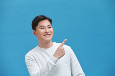 Yakışıklı genç adam mavi arka planda dikilirken işaret ediyor.