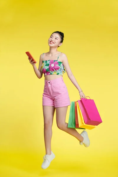 亚洲女人用手机 提着购物袋在黄色上面 — 图库照片