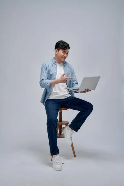 彼のラップトップを指している間に自信を持って笑顔で椅子に座っている大人のアジア人男性 — ストック写真