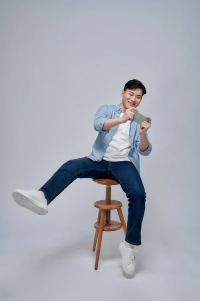 興奮した若い男の肖像画がスツールに座って携帯電話でゲームをプレイ — ストック写真