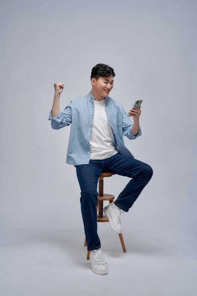 若いアジアの男は 携帯電話のアプリケーションでゲームをプレイし 成功を祝うと腕を上げる — ストック写真