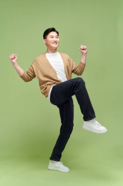 Başarıyı kutlayan genç bir adamın tam uzunluğu yeşil arka planda izole edilmiş.