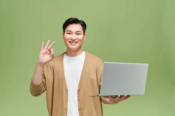 笑顔や幸せなアジア人男性ジェスチャー手 を行うか 緑の背景にノートパソコンを保持 — ストック写真