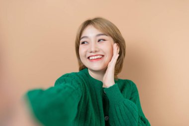 Makyajlı güzel esmer kız bej renkli bir stüdyoda özçekim yapıyor.