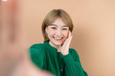 Duygusal olarak mutlu, neşeli, güzel bir kadının bej duvar arkasında izole bir şekilde poz vermesi kamera tarafından selfie çekiliyor..