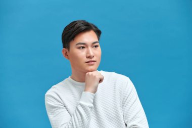 Genç yakışıklı, çekici, düşünceli adam kameraya bakıyor, el ele tutuşup çenesini tutuyor.