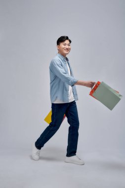 Genç pozitif adam alışveriş çantalarını tutuyor. Reklamlardan memnun.