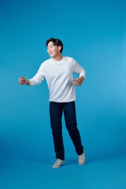 Mavi arka planda yalnız dans eden genç Asyalı adam.