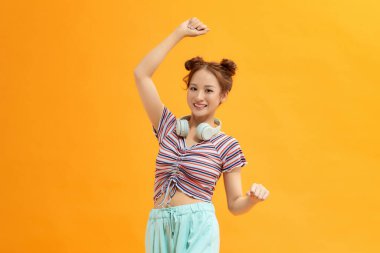 Boynunda kulaklıkla, yüzünde bir gülümsemeyle dans eden neşeli bir kadının portresi.