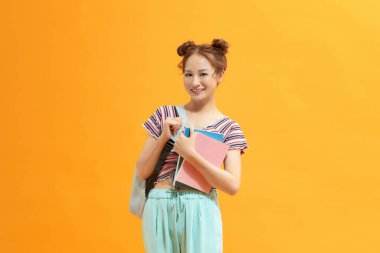 Sırt çantası takan genç bir bayan izole edilmiş sarı arka planda kitapları tutuyor..